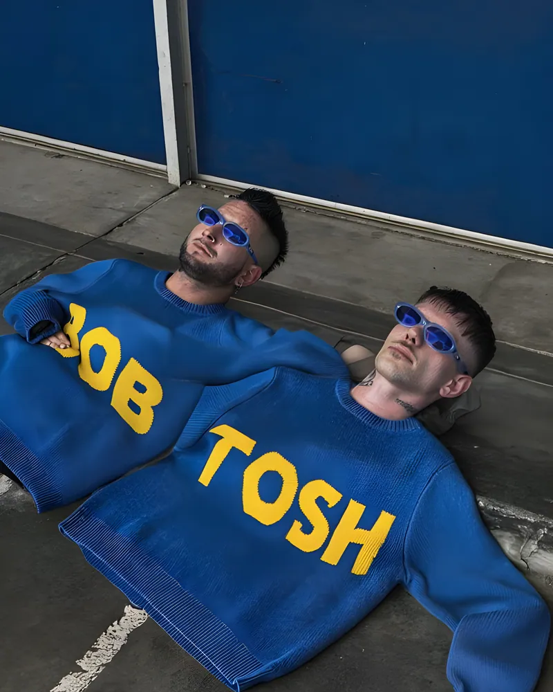 El dúo tirado en el piso con un buzo azul que dice BOB TOSH